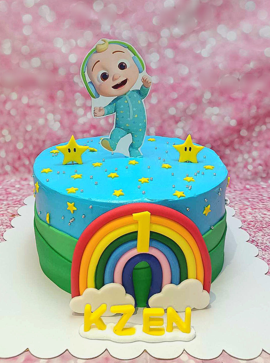 This delightful Cocomelon Cake features a light blue design adorned with stars and a colorful rainbow, celebrating a baby boy's 1st birthday. The cake showcases Jayjay from Cocomelon and is topped with the number 1, perfect for a one-tier celebration.