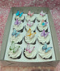 A beautifully decorated cake with white icing showcases an arrangement of pastel color assorted butterflies and printed cupcake toppers. Perfectly complemented by matching cupcakes, this design is ideal for any celebration.