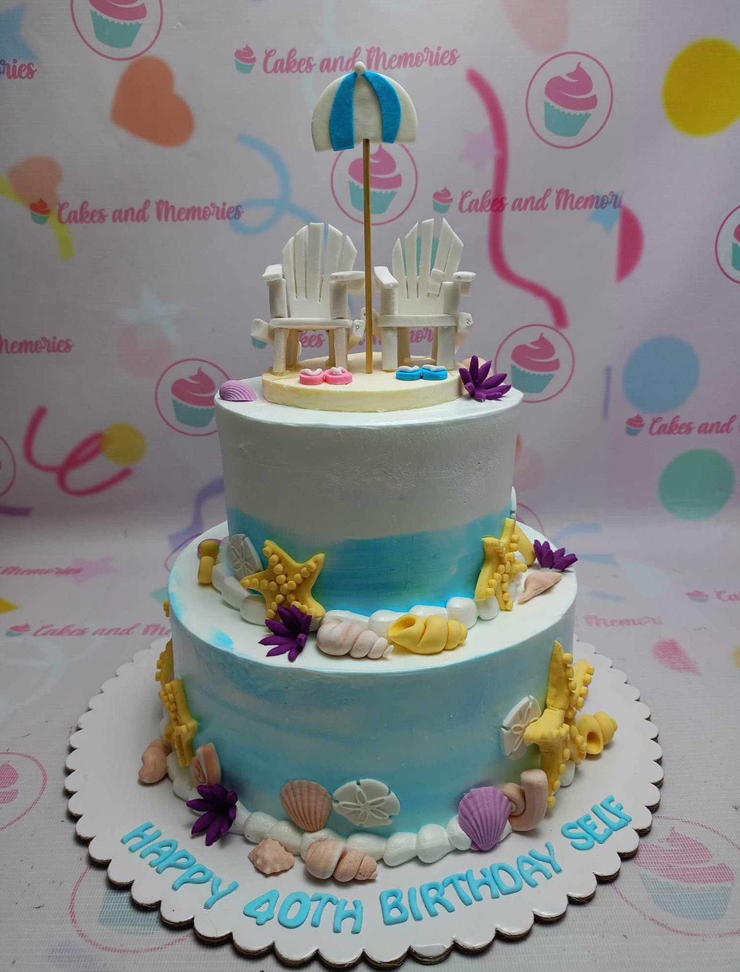 This stunning two-tier beach cake features a white and blue color scheme, adorned with intricate details like sand, seashells, corals, and a playful umbrella beside a mini folding chair. Perfect for summer birthdays, it captures the essence of a relaxing day by the ocean with elements like a snorkel and starfish.