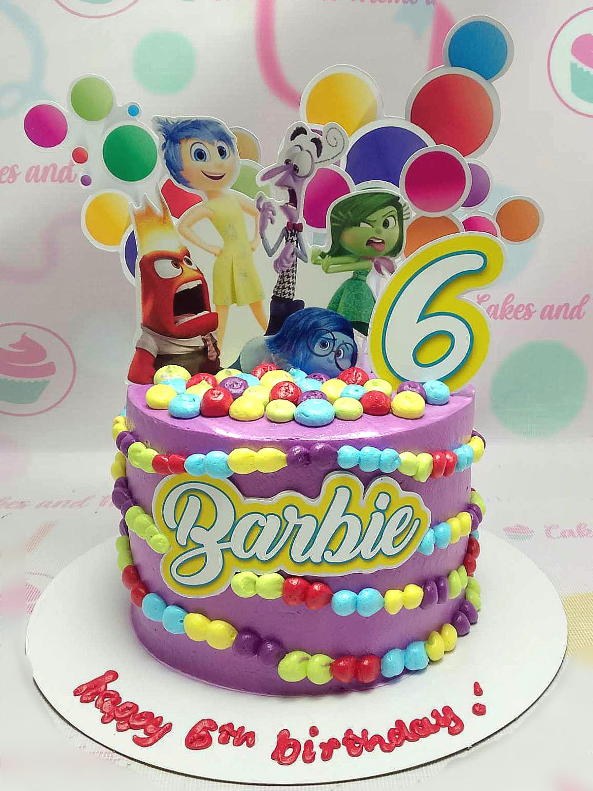 This 1-tier Inside Out Cake features rich purple icing adorned with colorful spheres representing Anger, Joy, Fear, Sadness, and Disgust, perfect for a Barbie-themed 6th birthday celebration inspired by Pixar. A delightful centerpiece for any child's special day, captured in a stunning photo uploaded in October 2024.