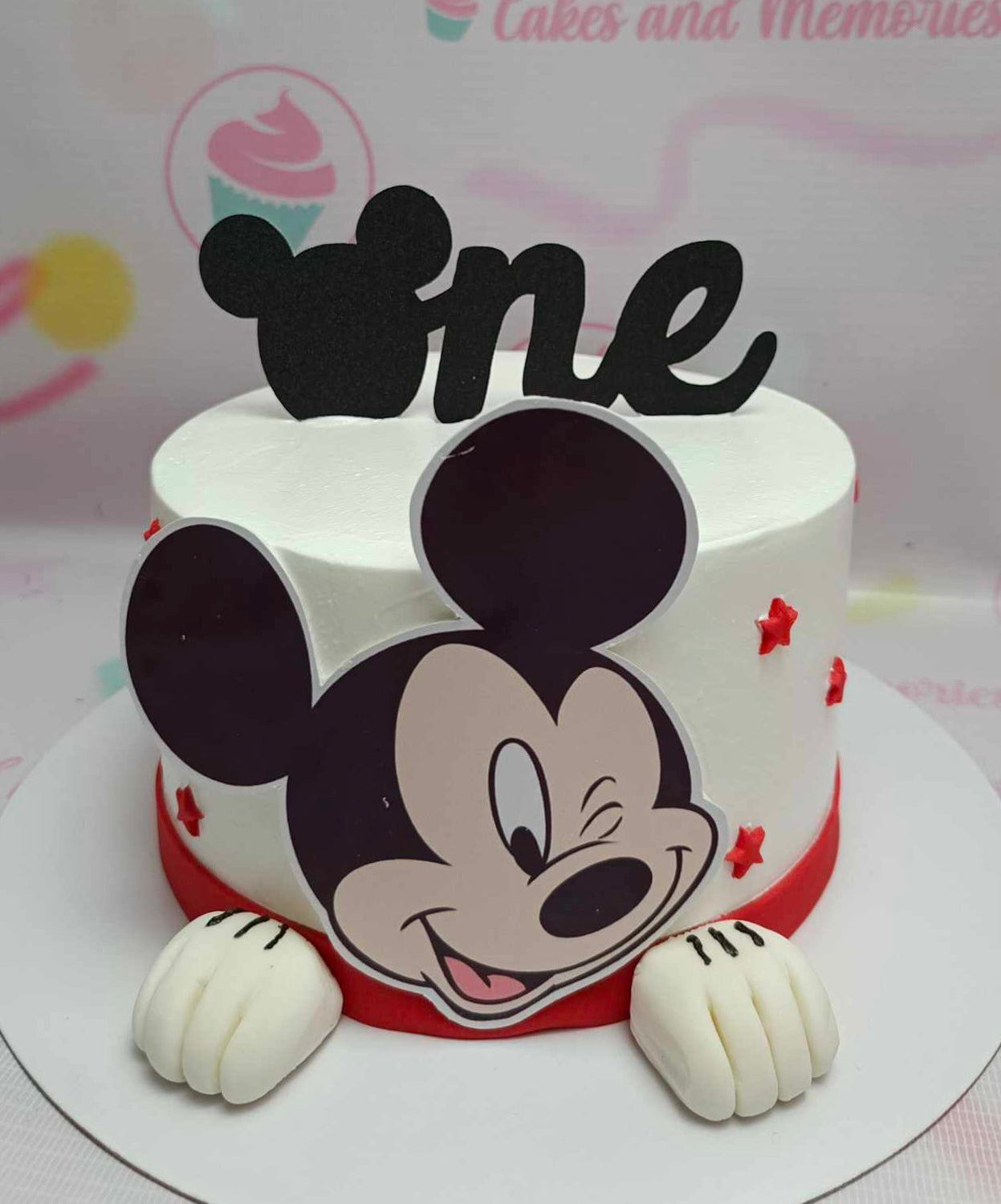 This vibrant one-tier Mickey Mouse cake features a classic white base adorned with a playful red ribbon and colorful printout toppers of beloved cartoon characters. Perfect for birthdays, this customized cake is a delightful choice for kids who love Mickey Mouse and his friends.