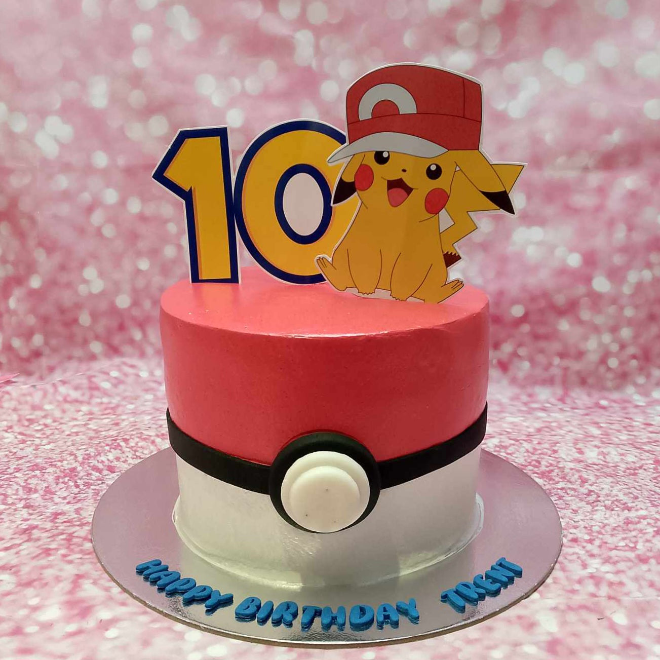 This custom Pokemon cake features a cheerful Pikachu and Pokeball design, perfect for a 10th birthday celebration for Trent. Adorned with red and white icing and playful printout toppers, it showcases a single layer and tier design.