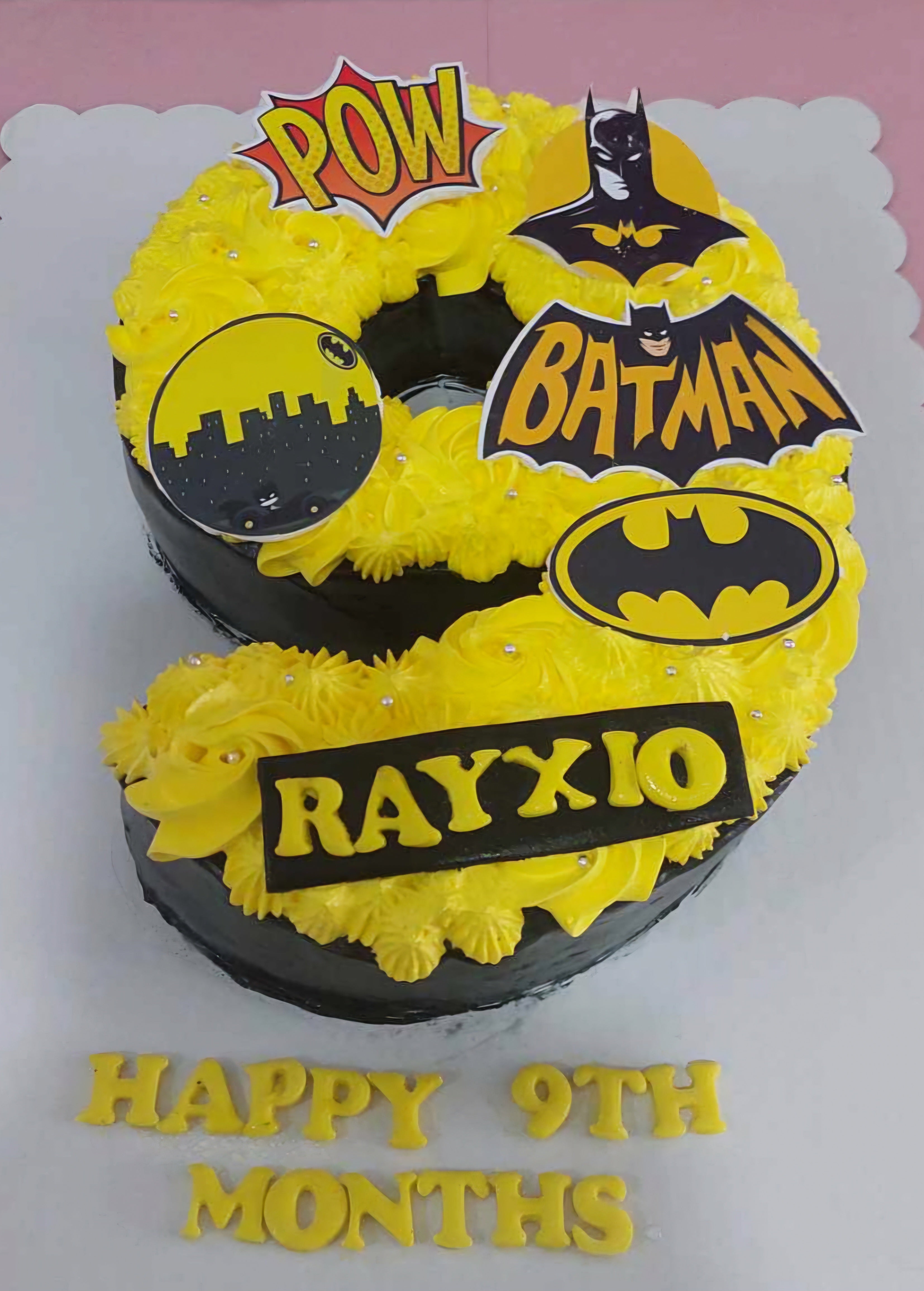 This custom Batman Cake features a striking yellow and black color scheme, shaped as the number 9, perfect for celebrating a 9-month milestone for a baby boy. The rectangular design showcases the iconic symbols of the Caped Crusader from DC Comics.