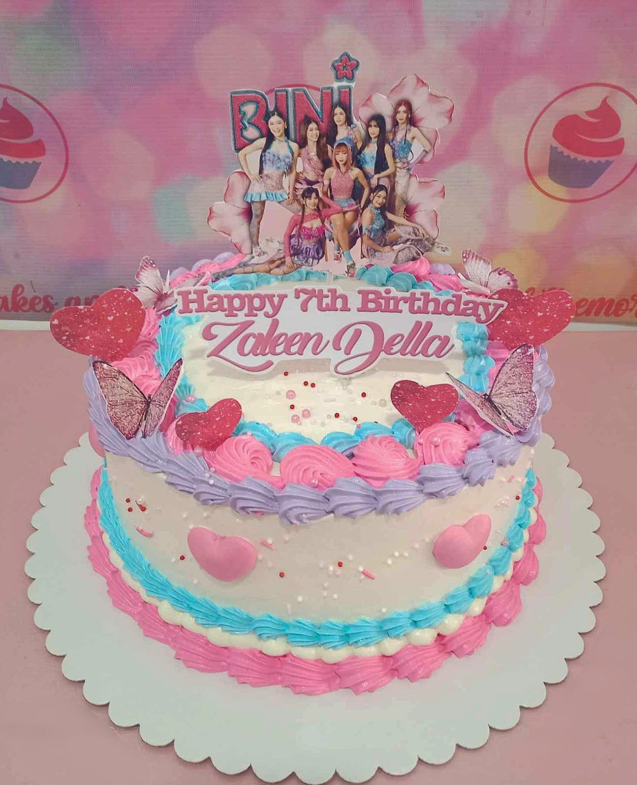 The Bini Cake features a stunning combination of pink, blue, and white, adorned with playful sprinkles, charming hearts, and delicate flowers, perfect for a cute, girly 7th birthday celebration. Accented with butterfly details and floral blooms, this single-tier cake captures the essence of ppop and kpop, showcasing a delightful tribute to beloved OPM artists.