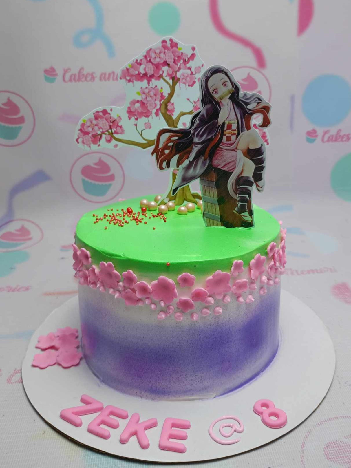 This stunning one-tier Demon Slayer cake features vibrant green, pink, and purple hues adorned with delicate cherry blossom accents. Custom printout toppers of Nezuko and other beloved characters from Kimetsu no Yaiba make it a perfect birthday cake for anime fans.