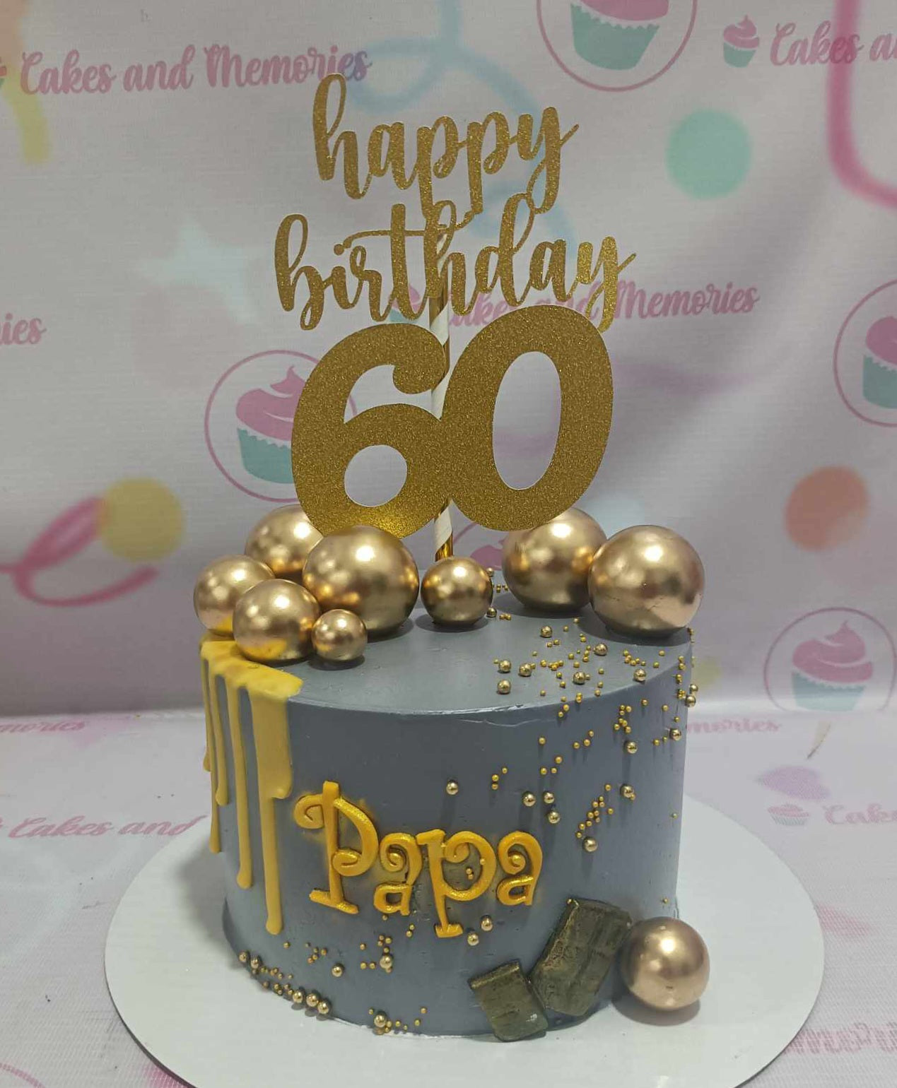 This custom Dad Cake features a sleek gray design with elegant gold accents, perfect for celebrating a 60th birthday. Adorned with a golden topper and gold drip, it showcases printout toppers and gold balls, creating a striking tribute for a beloved grandfather or father.