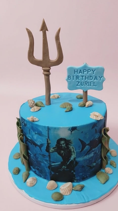Aquaman themed birthday cake with edible photo, trident topper, and seashell decorations for a 7th birthday.