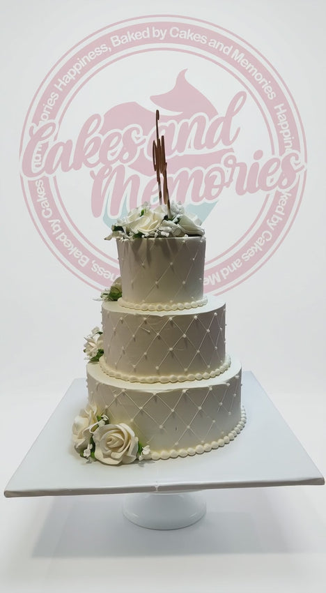 Elegant 3-tier white wedding cake with quilted pearl design, white roses, and gold monogram topper