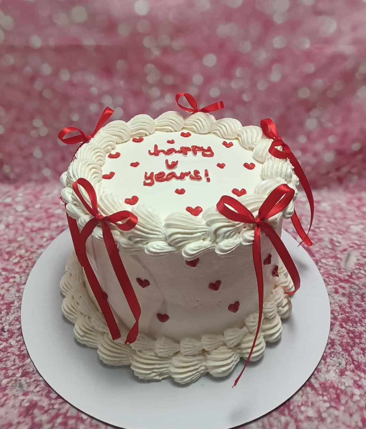 Anniversary cake with white buttercream, red heart sprinkles, 'Happy V Years!' text, and red ribbon bows.