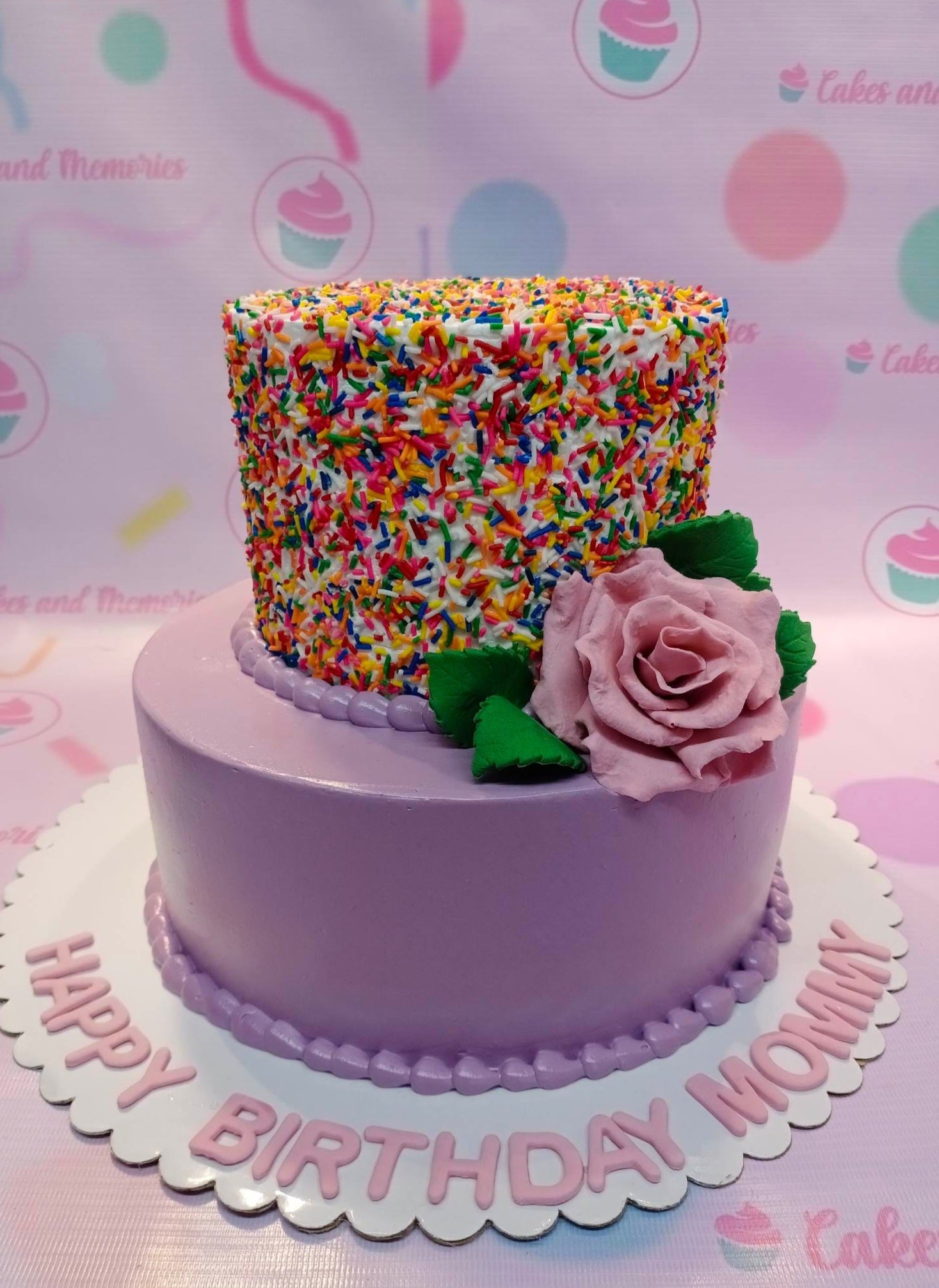 This delicious cake is a custom creation perfect for a special occasion. The cake features a beautiful floral design, with colorful rainbow and purple rose accents surrounded by a delightful sprinkle of candy. The perfect cake for a special 18th birthday or a mother's day.
