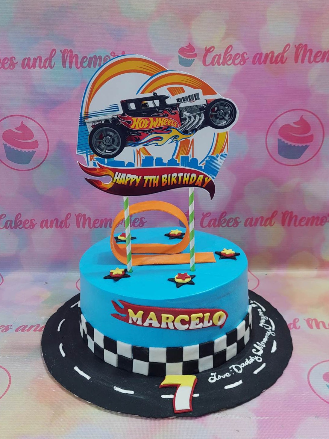 This Hotwheels Cake is perfect for any kid's birthday! It features a checkered race-track design decorated with a hot wheels car, and accented with orange and blue. Made with premium ingredients, this custom cake is sure to excite any young racing fan.